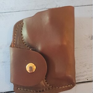 May include: A brown leather holster with a gold button closure.