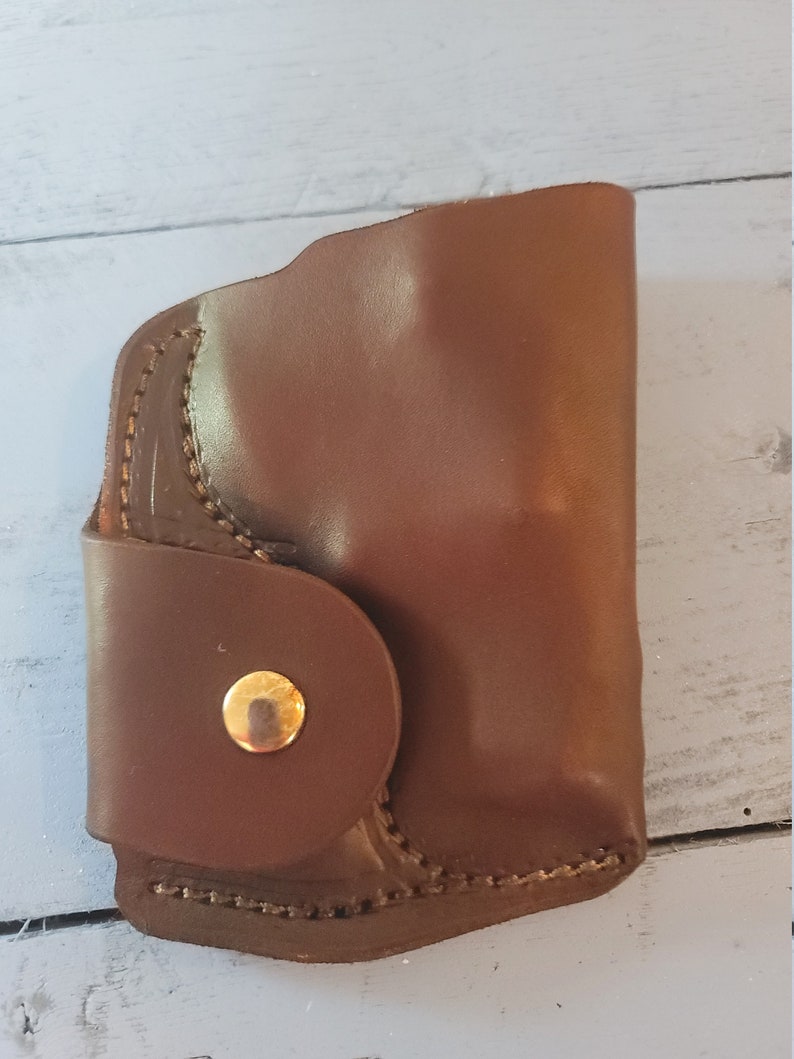 May include: A brown leather holster with a gold button closure.