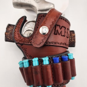 May include: A brown leather holster with a silver revolver and a blue and turquoise bullet holder. The holster has the word "MI" embossed on it.