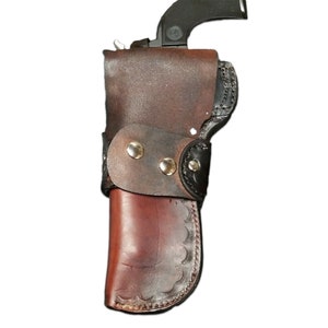 Puede incluir: Una funda de cuero marr&oacute;n con una correa de cuero negro y remaches plateados. La funda est&aacute; dise&ntilde;ada para sostener un arma de fuego.