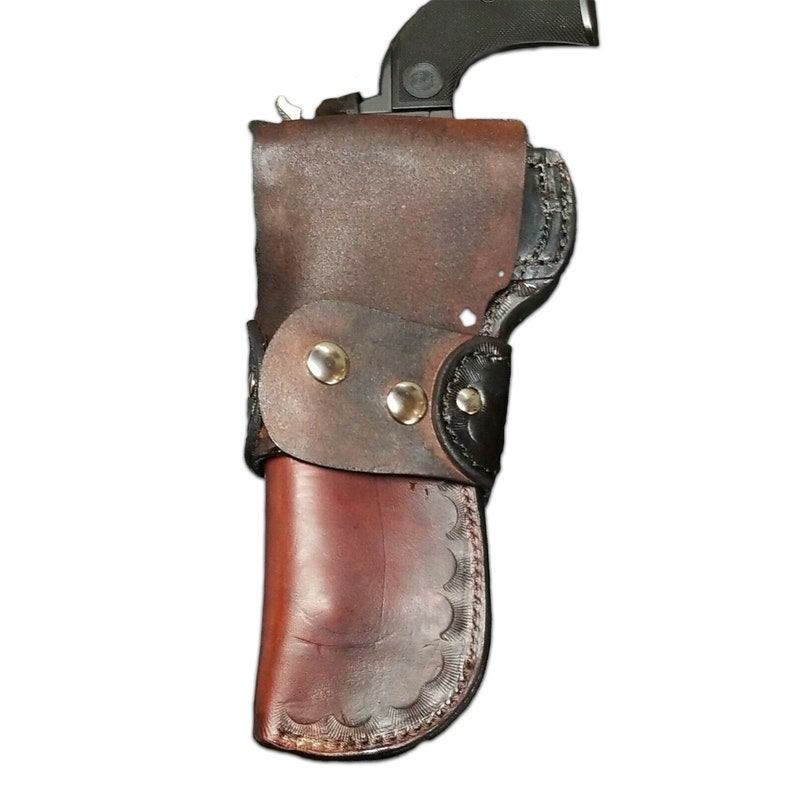 Puede incluir: Una funda de cuero marr&oacute;n con una correa de cuero negro y remaches plateados. La funda est&aacute; dise&ntilde;ada para sostener un arma de fuego.