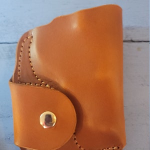 May include: A brown leather wallet with a snap closure and a stitched design. The wallet has a single button on the front.