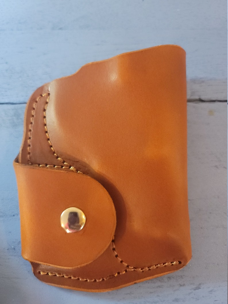 May include: A brown leather wallet with a snap closure and a stitched design. The wallet has a single button on the front.