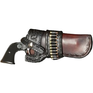Puede incluir: Una funda de cuero negro con una solapa de cuero marr&oacute;n y una hebilla plateada. La funda est&aacute; dise&ntilde;ada para sostener un rev&oacute;lver y tiene un lazo para un cintur&oacute;n. La funda est&aacute; decorada con un patr&oacute;n floral y las iniciales "A.S." est&aacute;n grabadas en el lateral. Una fila de balas es visible en el lateral de la funda.