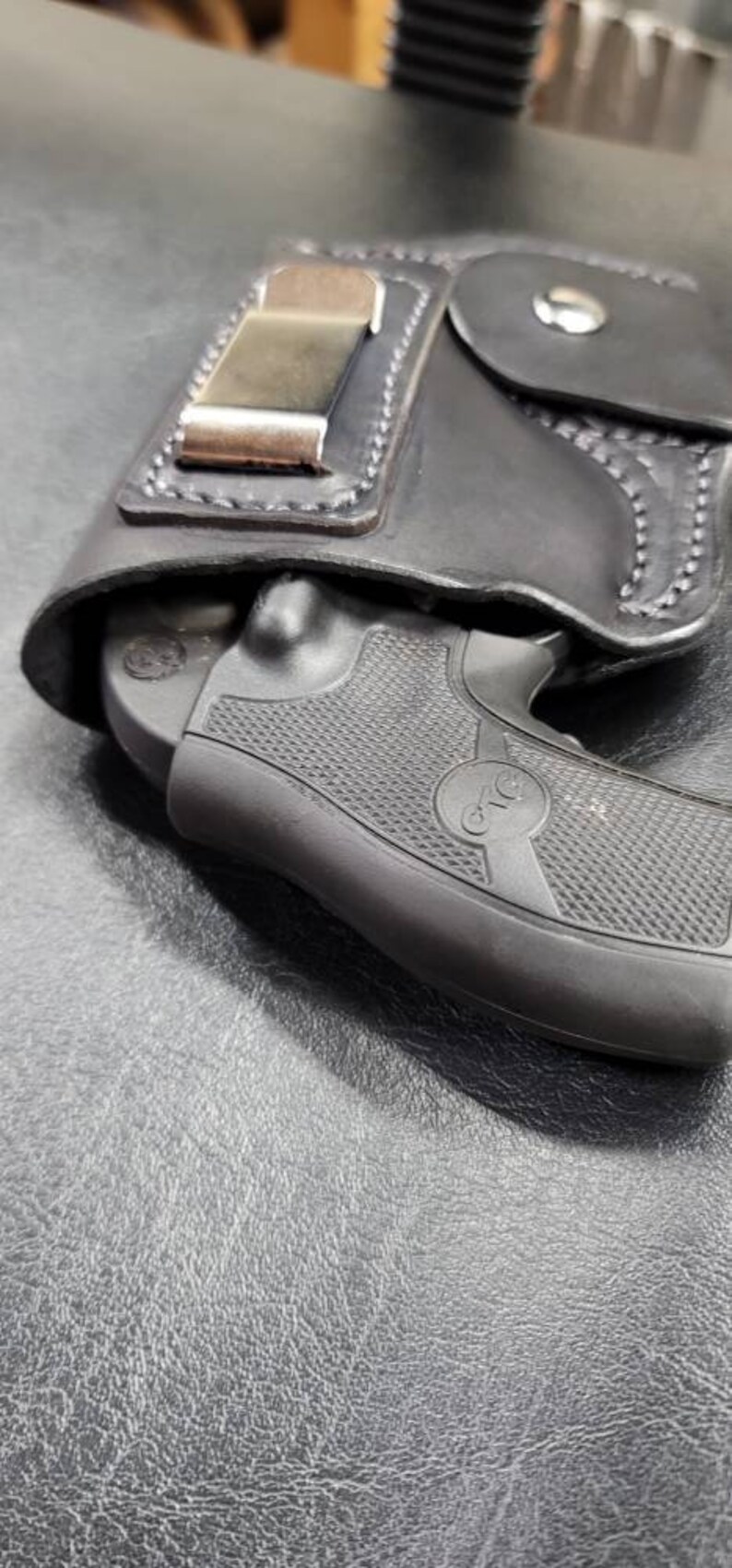 May include: A black leather holster with a silver clip for a small black handgun. The gun has a textured grip and a circular logo that says "CTG".