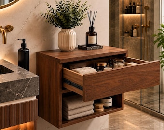 May include: A wall-mounted dark wood bathroom vanity featuring one open drawer and one open shelf. The drawer contains small containers and towels, while the shelf holds folded towels and a jar. A ribbed vase with greenery sits on top.