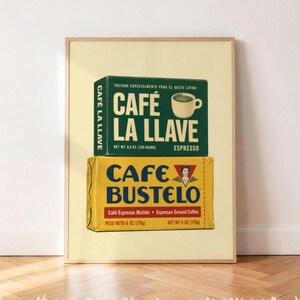 May include: A framed print featuring two stacked coffee bricks. The top green brick is labelled CAFÉ LA LLAVE ESPRESSO with a coffee cup graphic and net weight 250 grams. The bottom yellow brick is labelled CAFÉ BUSTELO with a portrait logo.