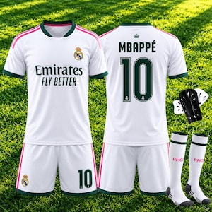 Può includere: Un completo da calcio bianco composto da una maglia con dettagli verde scuro, strisce rosa sulle spalle e la scritta Emirates Fly Better. Sul retro sono presenti il nome Mbappe e il numero 10. Include pantaloncini abbinati, parastinchi neri e calzettoni bianchi.