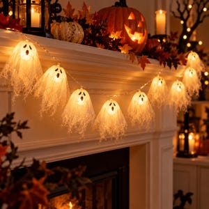Pode incluir: Um cordão de luzes LED com várias coberturas brancas em forma de fantasma feitas de tecido fino e vaporoso. Cada fantasma tem um rosto preto simples com dois olhos e uma boca aberta. As luzes emitem um brilho quente e festivo.