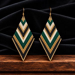 May include: A pair of diamond-shaped dangle earrings crafted from small beads in a chevron pattern. The beads feature a color palette of metallic gold, deep forest green, cream, and matte black, suspended from simple gold-toned metal earring hooks.