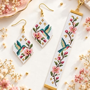 May include: A set of two diamond-shaped beaded earrings and a matching rectangular beaded bracelet. Each piece features a white background with a pattern of pink flowers, green leaves, and a hummingbird, accented with small gold-colored stars.