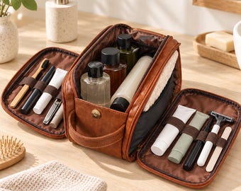 May include: A brown leather toiletry bag with a wide opening, featuring internal elastic loops holding various grooming items like toothbrushes, razors, and bottles. The bag is labeled with the text Spacious Storage.
