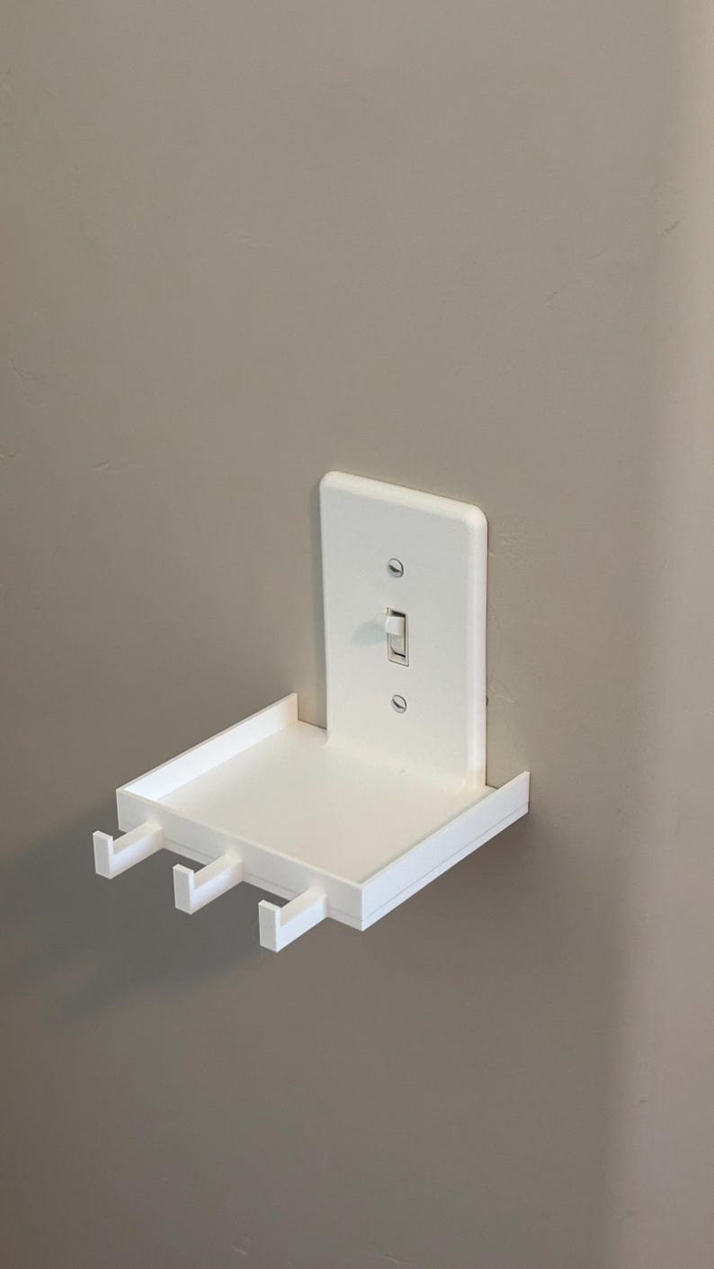 Puede incluir: Un estante de pared de pl&aacute;stico blanco dise&ntilde;ado para encajar sobre un interruptor de luz est&aacute;ndar. El estante rectangular cuenta con una superficie plana y tres peque&ntilde;os ganchos en el borde frontal para colgar objetos.