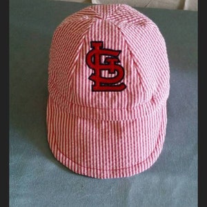May include: A pink and white striped baseball cap with a red and black embroidered "S" on the front.