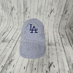 Può includere: Un berretto da baseball a righe blu e bianche con le lettere "LA" ricamate in blu scuro sul davanti.