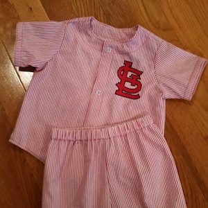 May include: A pink and white striped baby pajamas with a red embroidered "LS" logo on the shirt.
