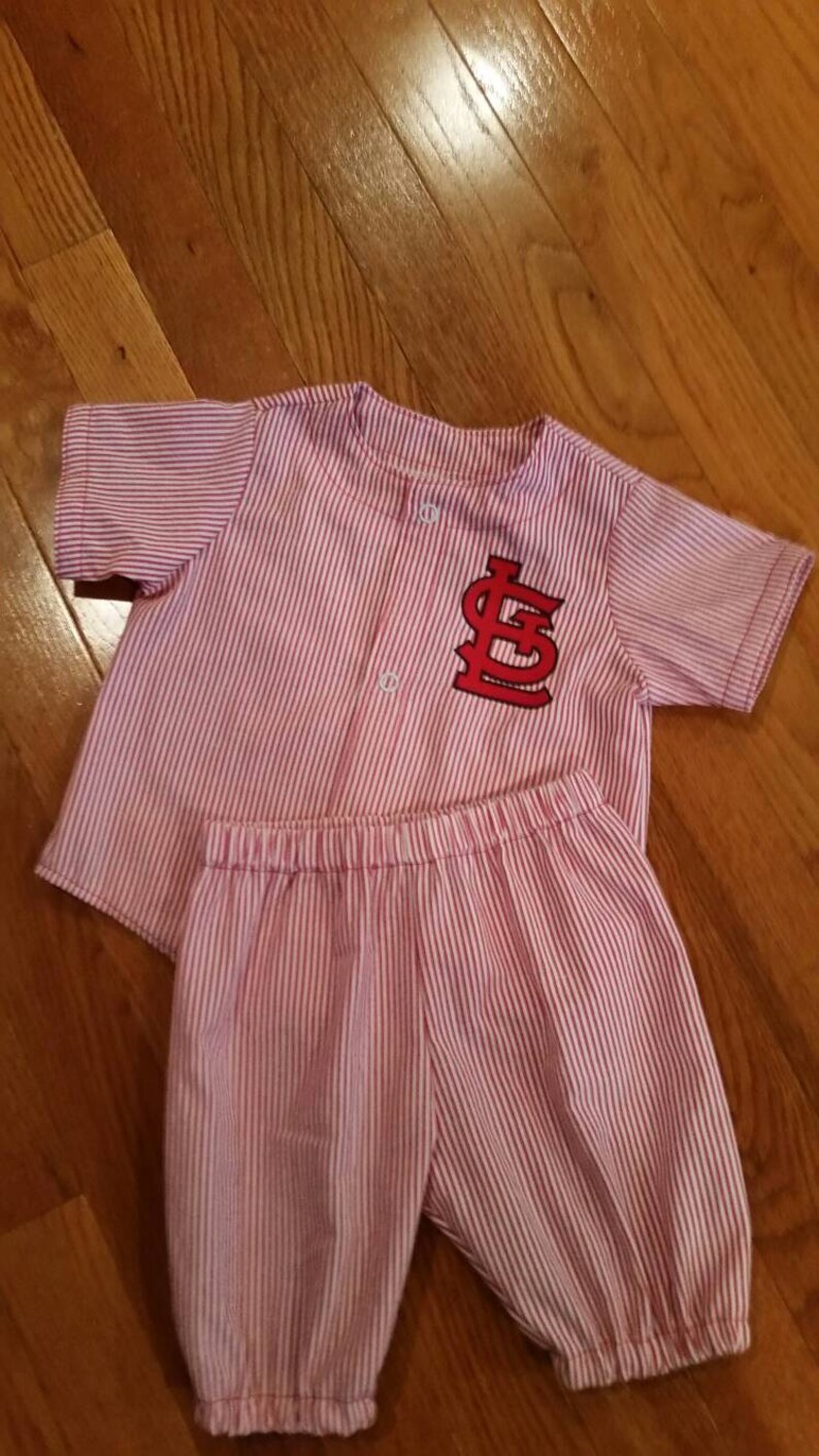 May include: A pink and white striped baby pajamas with a red embroidered "LS" logo on the shirt.
