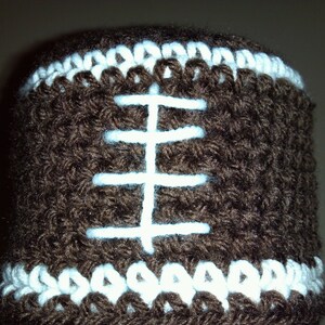 Può includere: Copertura per rotolo di carta igienica in crochet marrone con dettagli in crochet bianco che ricordano un pallone da calcio.