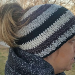 Può includere: Un cappello a crochet a righe nere, grigie e bianche con un foro nella parte superiore per una coda di cavallo.