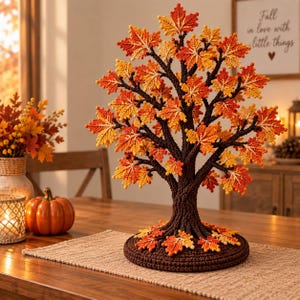 Puede incluir: Un árbol decorativo de ganchillo con un tronco y una base de color marrón oscuro, adornado con numerosas hojas de arce de colores otoñales vibrantes en tonos rojos, naranjas y amarillos. Las hojas están unidas a ramas marrones y dispersas en la base.