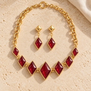 May include: A gold-tone necklace and matching drop earring set featuring faceted, diamond-shaped red stones. The necklace consists of a thick chain link design with seven red stone pendants, while the earrings feature a single matching stone.