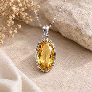 May include: A silver pendant necklace featuring a large, oval-cut yellow gemstone set in a twisted rope-style metal frame. The pendant hangs from a delicate silver chain, showcasing a faceted surface that reflects light with clarity.