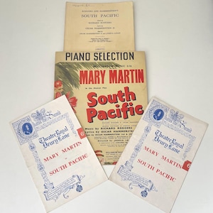 May include: A collection of three South Pacific musical paper items including a libretto, a piano selection sheet music book featuring Mary Martin, and two Theatre Royal Drury Lane programmes with blue decorative borders and red text.