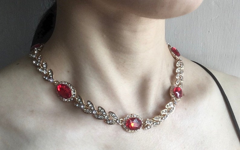 May include: A gold necklace with a delicate leaf design and red gemstone accents. The necklace features a larger oval-shaped red gemstone in the center.