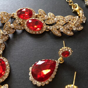May include: A gold-tone necklace with red and clear crystal stones. The necklace features a leaf design and is paired with matching earrings.