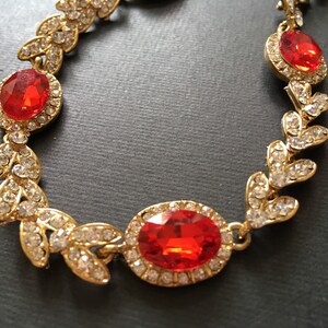 May include: Gold tone necklace with red and clear rhinestones in a leaf design.