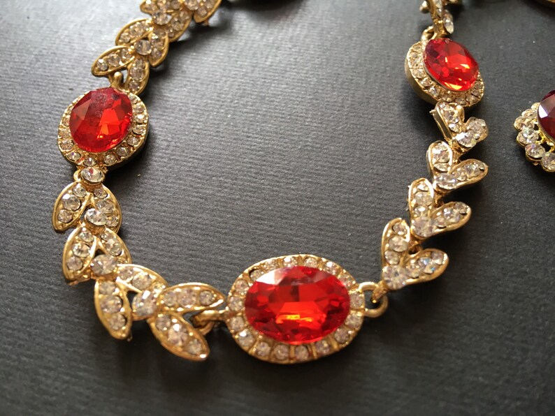 May include: Gold tone necklace with red and clear rhinestones in a leaf design.