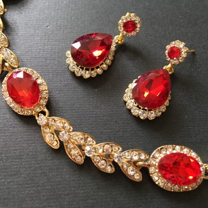 May include: A gold necklace and earrings set with red teardrop-shaped stones surrounded by clear rhinestones. The necklace features a leaf design.