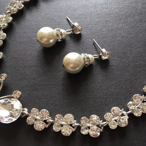 Puede incluir: Un conjunto de collar y pendientes plateados con detalles de cristal transparente y perlas de imitaci&oacute;n. El collar presenta un dise&ntilde;o de mariposa y racimos florales. Los pendientes tienen perlas colgantes y tachuelas de cristal.