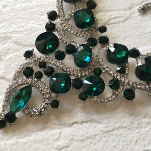May include: A silver-toned necklace featuring large emerald green faceted crystals, smaller round black stones, and clear pav&eacute; rhinestones set in a swirling metal frame. The design incorporates various shapes including marquise and round cuts.
