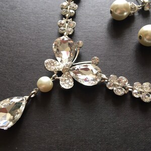Puede incluir: Un conjunto de joyas plateadas que incluye un collar y pendientes a juego. El collar presenta un colgante en forma de l&aacute;grima y un dise&ntilde;o de mariposa con cristales transparentes y brillantes. Los pendientes son de tipo perla.