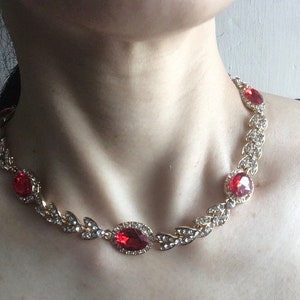 May include: A gold necklace with a delicate leaf design and red gemstone accents.