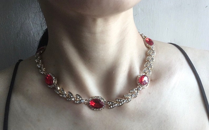 May include: A gold necklace with a delicate leaf design and red gemstone accents.