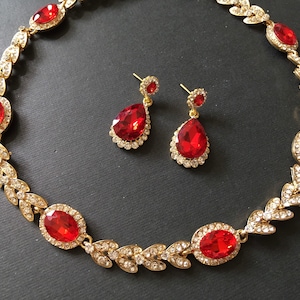 May include: A gold necklace with red crystal stones and matching earrings. The necklace features a leaf design with small crystals.