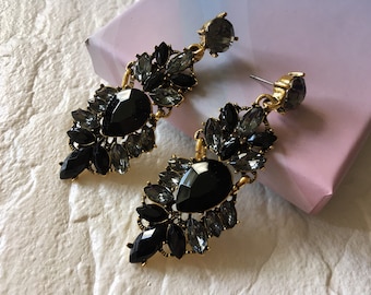 May include: A pair of dangle earrings with black and gray rhinestones. The earrings are gold-toned and have a teardrop shape.