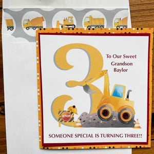 May include: A birthday card with a construction theme. The card features a large yellow number 3 with a construction vehicle. Text reads "To Our Sweet Grandson Baylor" and "Someone Special is Turning Three!!". The envelope has construction vehicle graphics.