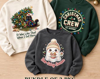 May include: Three crewneck sweatshirts in cream, dark green, and charcoal grey. The cream sweatshirt features a black cat tangled in Christmas lights with the text It Was Like That When I Got Here. The green one says Christmas Crew Est. December. The charcoal one shows a ghost in a winter hat holding a mug with the text Boo-liday Season.