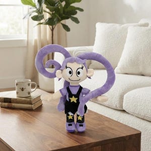 May include: A plush doll featuring a character with long, curled purple hair, large eyes, and a smiling expression. The doll wears a purple shirt, black overalls with a yellow star on the chest, and purple shoes with yellow star accents on the legs.