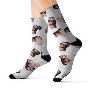 May include: White socks with a repeating pattern of a person wearing sunglasses. The socks have black heels and toes. The pattern features a person with sunglasses and a neutral skin tone.