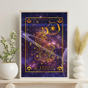 Puede incluir: Impresión artística enmarcada con el signo zodiacal de Acuario. La obra de arte representa una ilustración dorada del símbolo de Acuario sobre un fondo cósmico de color púrpura, azul y dorado. La palabra "ACUARIO" está escrita en dorado en la parte inferior.