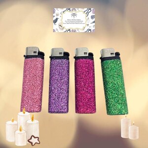 May include: Four lighters with glitter covers in pink, purple, magenta, and green. The lighters are on a light brown surface with white candles.