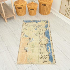 May include: A rectangular area rug featuring a faded, distressed pattern in shades of beige, cream, and light orange, with a prominent deep blue border along the right side and top edge, decorated with small, scattered floral and geometric motifs.