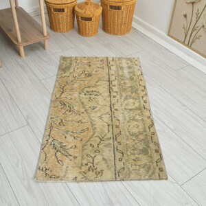 May include: A rectangular area rug featuring a faded, distressed pattern in muted shades of beige, tan, and sage green. The design includes intricate floral motifs and geometric borders, with a weathered texture throughout the woven surface.