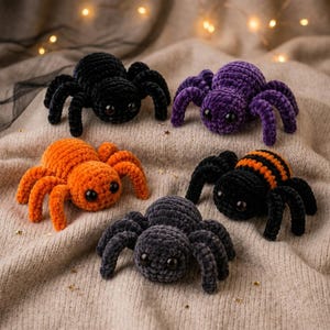 May include: Five plush crochet spiders with large black eyes. The spiders are colored solid black, solid purple, solid orange, solid dark gray, and one black spider with orange stripes. Each spider has eight legs and a soft, fuzzy texture.
