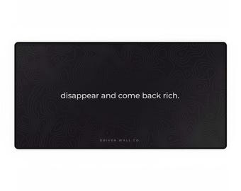 May include: A rectangular black desk mat featuring a dark gray topographic map pattern. The text "disappear and come back rich." is printed in white in the center, with "DRIVEN WALL CO." printed in smaller white text at the bottom.