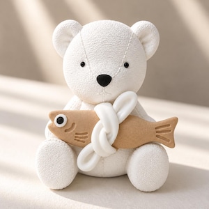 May include: A white textured bear figurine with small black eyes and a black nose. The bear is holding a tan-coloured fish in its arms, which is secured by a white knotted loop. The bear has visible stitched seams on its head and body.